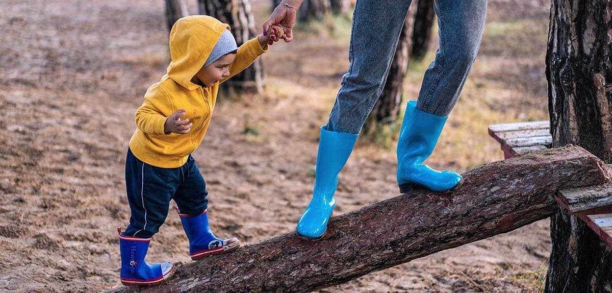 Image of child being helped by an adult to walk across a log