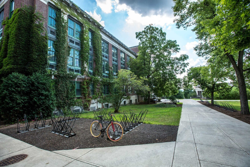 a beautiful view of the front of a school building lined with trees and a bike on bike stands in front