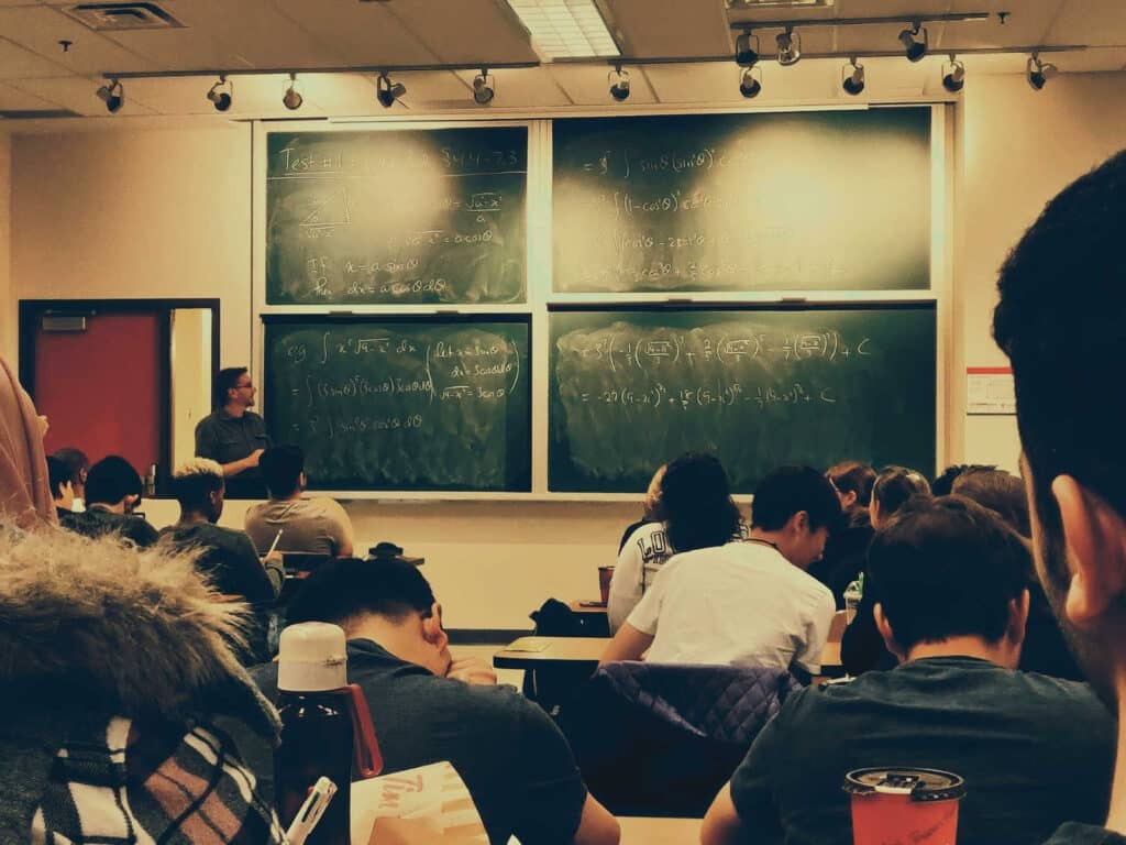 view of a classroom with students and a lecturer in front looking at the board with equations