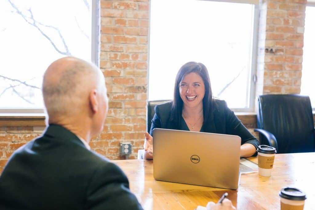 Image of woman laughing with coworker at a desk area with her laptop.