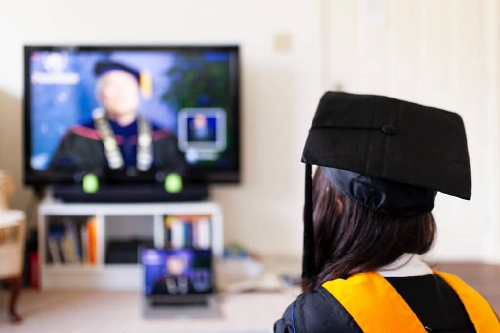 Image of a graduating student watching a live stream of their graduation on a TV.
