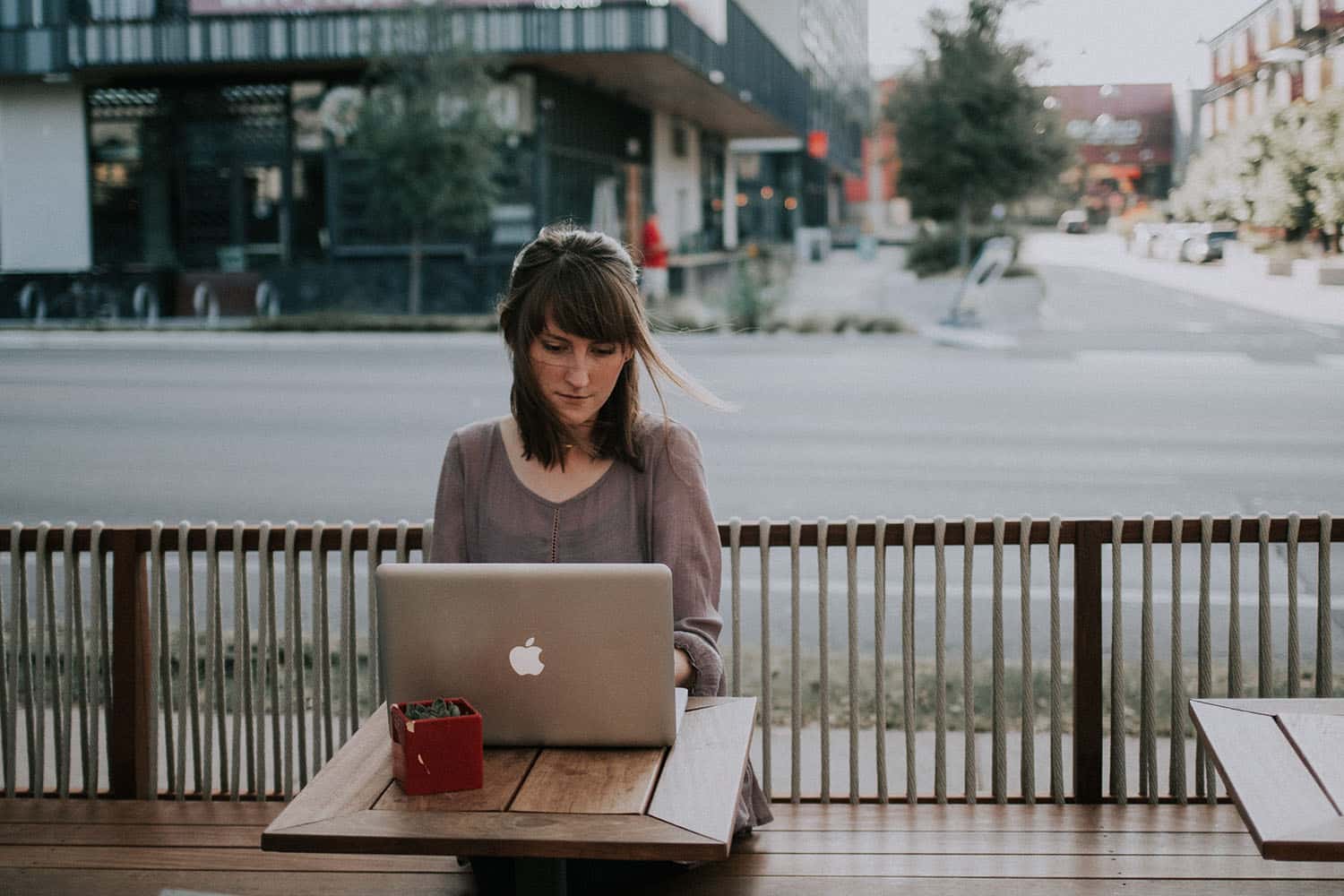 Image of a woman using her laptop while sitting on a table outside.