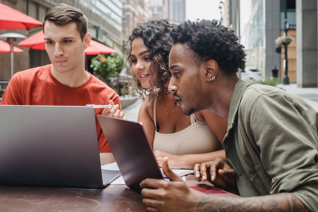 Image of three students looking at their laptop screens together.
