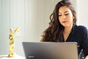 Woman sitting at a desk and looking down at her laptop screen.