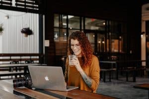 Image of a woman sitting at a table with her laptop and an iced coffee.
